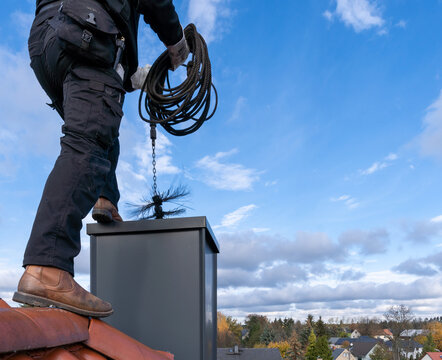 Chimney sweep man in work uniform cleaning chimney on building roof
