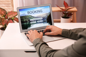 Man with laptop booking tickets online at white table, closeup. Travel agency concept