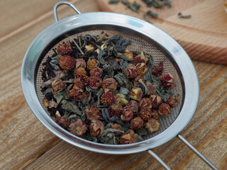 Dried wild strawberries in a metal sieve close-up. Healthy berries and herbs on a wooden table. Tea with berries