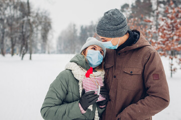 Fototapeta na wymiar Man gives gift box to his girlfriend for Valentines day in snowy winter park. Couple wear masks. Coronavirus covid