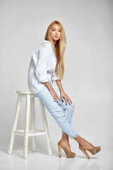 beautiful blonde woman with long hair in jeans and a white shirt sitting on chair and looking at...