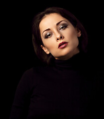 Fototapeta premium Sexy woman with bright evening makeup, red lipstick brown brow posing isolated on dark black background. Closeup portrait in deep low key light shadows. Art.