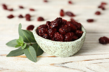 Tasty dried cranberries and leaves on white wooden table
