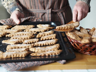 Homemade cookie concept. The hands of an elderly woman remove the prepared freshly baked cookies from the baking sheet onto a plate.Blurred foreground.