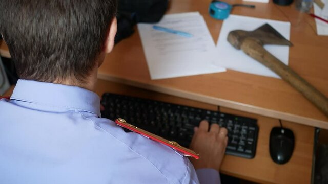policeman examines weapon ax typing on keyboard in uniform