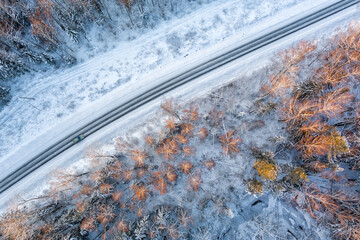 Aerial view from drone of car on a curvy snow covered road in the winter forest