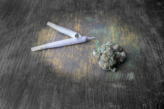 Buds of marijuana, and cannabis rolled joints on black and white with colors wooden background.
