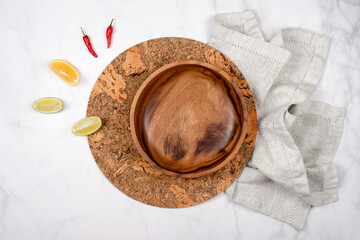 Empty wooden plate on a napkin and cork trivet heat with lemon and pepper. Dinner setting over light table background. Kitchenware utensils, wood plate and cutting board. Top view, copyspace