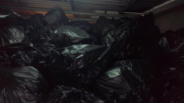 Pan shot inside dark metal dumpster filled with plastic trash garbage bags