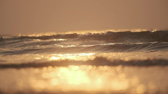 Small waves crashing on the sea shore at sunset beautiful golden hour slow motion