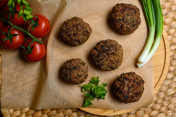 Homemade fried meatballs, served on wooden cutting board with tomatoes, onions and parsley