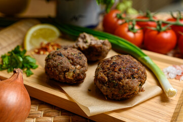 Homemade fried meatballs, served on wooden cutting board with tomatoes, onions and parsley