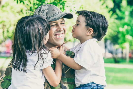 Caucasian man holding kids and smiling. Happy cute children hugging and kissing middle-aged father in military uniform. Dad returning from army. Family reunion, fatherhood and returning home concept
