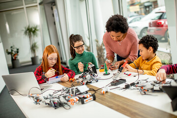 Happy kids with their African American female science teacher with laptop programming electric toys...