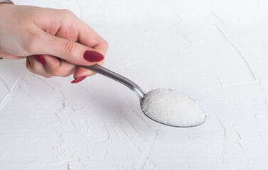 a spoonful of granulated sugar in the hands of a woman on a white background