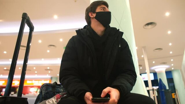 A masked man in black uses telephone in station using mobile Internet in application. Chooses the time of the road, the purchase of an electronic ticket.