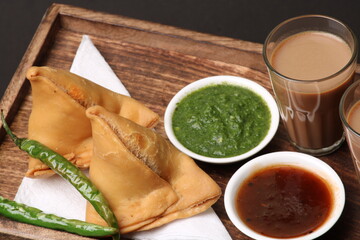 Indian snack Homemade spicy and delicious samosa served with green, tamarind chutney cutting masala tea, chai, 