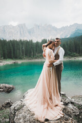 Wedding couple on the nature is hugging each other near a beautiful lake in the mountains.. Beautiful model girl in white dress. Man in suit