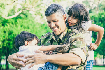 Happy disabled military dad walking with two children in park. Girl holding wheelchair handles, boy...