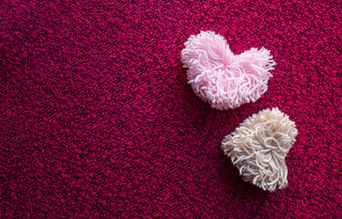 Two fluffy pompoms made of pink and beige heart-shaped ponies on a crimson background