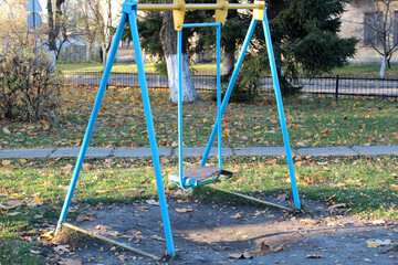 Fototapeta premium Old rusty abandoned broken swing, withered autumn grass, green and red shabby paint