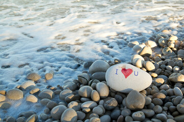 I love you and heart painted with a red paint marker on the pebble as a gift for Saint Valentine's day on the pebble background. Spontaneous symbol of love and passion. Copy space for text. 