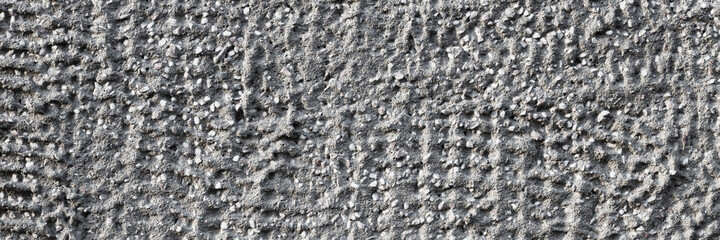 Texture of a decorative concrete wall. Rough gray surface with a grainy pattern of small stones and dents. Wide panoramic texture for background and design.