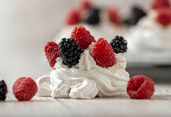 Merengue cake, decorated with raspberries and blackberries. Pavlova cake. Light wooden background. Home cooking.