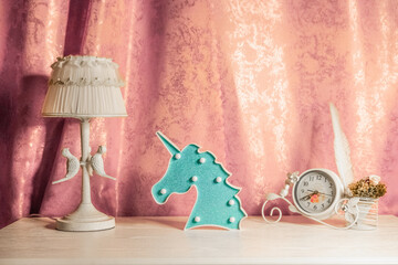 Blue unicorn sign and mramor lamp wuth birds around it and vintage clocks with bouqet and birds feather are standing on the table in the girls bedroom before the Valentine's Day