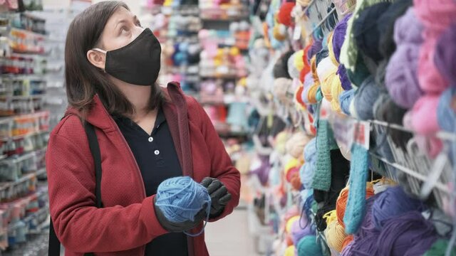Woman wearing a mask and gloves against the virus chooses chenille yarn for knitting and needlework. The concept of hobby and craft