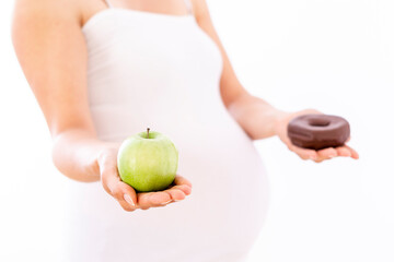Pregnant woman choosing healthy apple over unhealthy donut