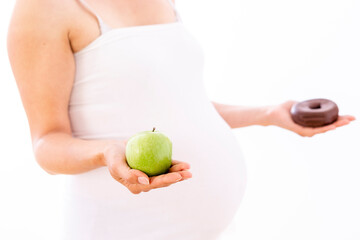 Pregnant woman choosing healthy apple over unhealthy donut