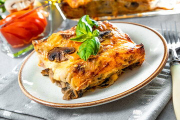  Piece of homemade vegetarian lasagna with mushrooms, tomatoes and basil on a plate close up
