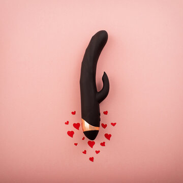 Black clitoral vaginal dildo and hearts on a pink background. Female vibrator as a gift for Valentine's Day