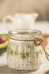 Natural yoghurt with Chia seeds and avocado in glass jar and white cream jug on white background . Detox and healthy superfoods. Side view.