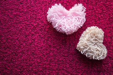 Two fluffy pompoms made of pink and beige heart-shaped ponies on a crimson background