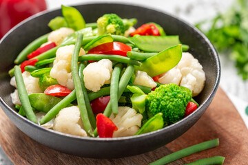 Cooked vegetables in a plate close-up. Steamed bean pods, pea pods, cauliflower, broccoli, and peppers. Healthy diet food, vegan food.