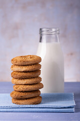 in the foreground, on the lavender blue table, a stack of biscuits with wholemeal flour and a bottle of cow's milk