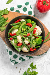 Cooked vegetables in a plate on a gray background top view.  Steamed bean pods, pea pods, cauliflower, broccoli, and peppers. Healthy diet food, vegan food.