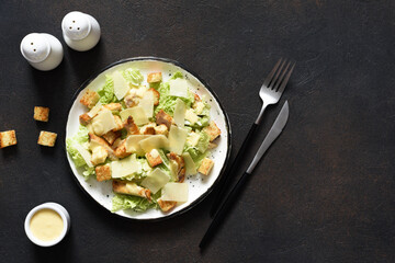 Classic Caesar salad with chicken and sauce in a plate on a concrete background, top view.