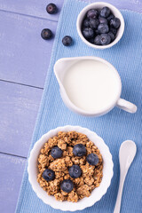 on lavender blue table, healthy breakfast with crunchy wholemeal muesli of barley and oats, blueberries and fresh milk. View from above.