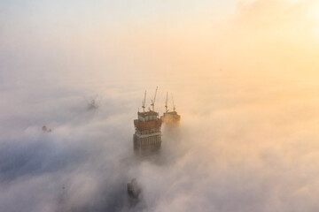 high rise skyscraper under construction covered in dense fog during sunrise