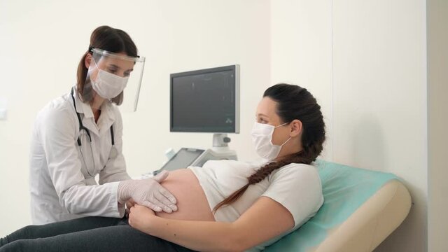 Doctor in mask and gloves examining tummy of pregnant woman