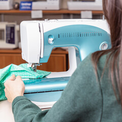 Woman works at blue sewing machine. Rear view
