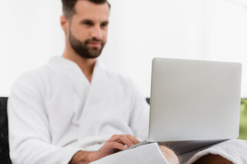 Laptop on laps of man in bathrobe on blurred background in hotel room