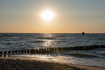 Sunset over the Baltic Sea. Vintage wooden breakwater in the waves. Mielno, Poland. Selective focus. 