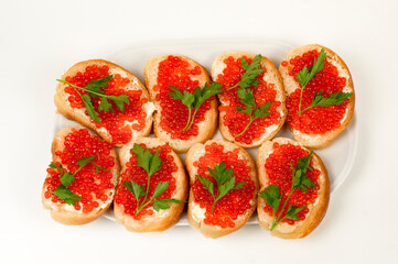 Six sandwiches with a loaf, red caviar and a sprig of herbs on a large white plate