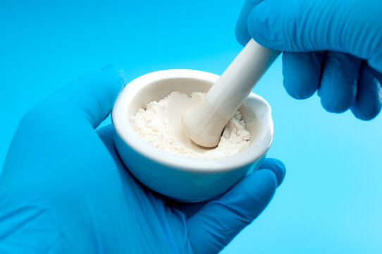 Pharmacy, pharmaceutical medication and medicinal preparation concept with pharmacist hands in gloves using mortar and pestle to ground fine white medicine blend isolated in science laboratory