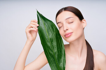A charming young brown-haired woman with bare shoulders holds a green sheet with her hands.