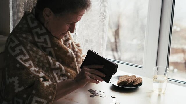 Elderly unhappy poor woman counting leftover coins in the kitchen at home